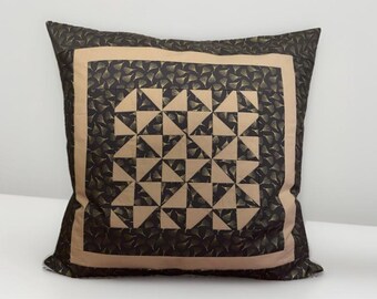 May include: Square decorative pillow with a geometric pattern. The pillow features a dark brown background with a repeating pattern of gold-colored fan-shaped designs. A tan border frames the central design of tan and dark brown triangles.