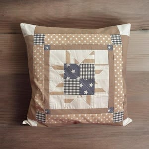 Könnte beinhalten: Quadratisches Zierkissen mit Patchwork-Design. Das Kissen hat ein zentrales Sternmuster mit blauen Stern- und Vichy-Quadraten, umgeben von beigem und weißem Stoff mit Tupfen. Das Kissen hat einen beigen Rand und weiße Ecken.