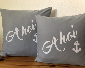 May include: Two grey throw pillows with white lettering that says "Ahoy" and a white anchor symbol.