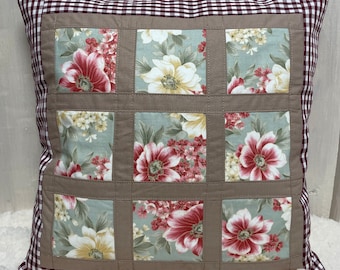 May include: A brown and white pillow with a red and white gingham border. The pillow is made of fabric with a floral pattern. The pillow is a patchwork of different floral fabrics.