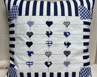 May include: A white pillow with a blue and white striped border. The center of the pillow is white with a pattern of blue hearts. The hearts are arranged in rows and are stitched with a wavy line.