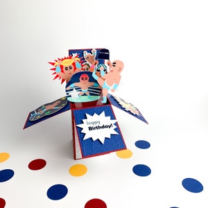 Puede incluir: Una tarjeta emergente azul y roja con tem&aacute;tica de lucha libre. La tarjeta presenta un ring de lucha libre con luchadores en el ring. La tarjeta est&aacute; abierta y el interior dice "&iexcl;Feliz cumplea&ntilde;os!"