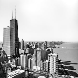 May include: A black and white aerial view of a city skyline with tall buildings and a body of water in the distance.
