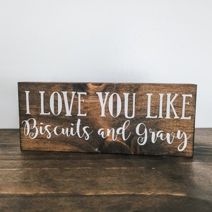 May include: A wooden sign with the text "I love you like biscuits and gravy" in white lettering.