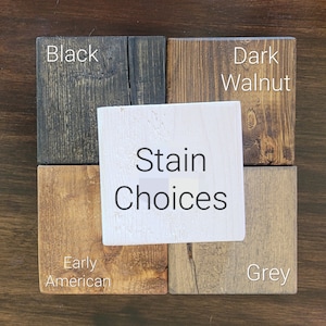 May include: A display of wood stain color options. The samples include Black, Dark Walnut, Early American, and Grey. A white square in the center reads "Stain Choices". The wood samples are arranged on a dark brown surface.