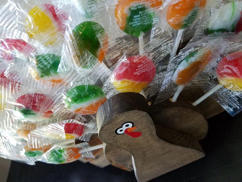 May include: A wooden turkey figurine with a painted face and red wattle, holding a variety of colorful lollipop candies wrapped in clear plastic.