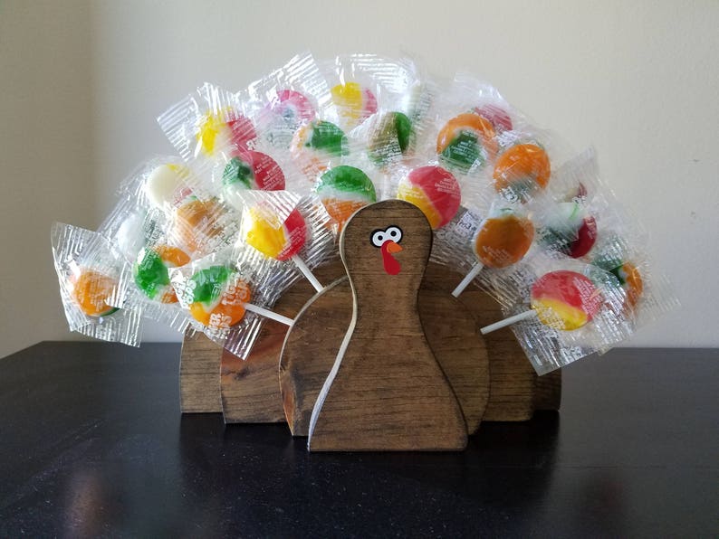 May include: A wooden turkey figurine with a brown and white painted design. The turkey has a colorful lollipop tail with red, yellow, green, and orange lollipops.