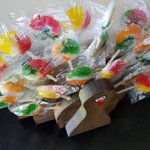 May include: A wooden turkey figurine with a red beak and eyes holds a variety of colorful lollipop candies wrapped in clear plastic.