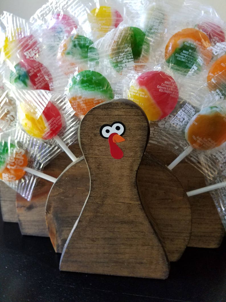 May include: A wooden turkey figurine with a red and white turkey head and eyes. The turkey is surrounded by colorful round lollipops wrapped in clear plastic.