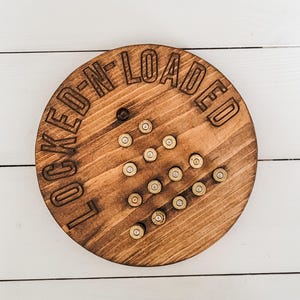 May include: A wooden round sign with the text "LOCKED N' LOADED" in a black font. The sign is decorated with a pattern of brass bullet casings.