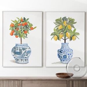May include: Two watercolour paintings of potted citrus trees. The painting on the left features a small orange tree with orange fruit in a blue and white porcelain pot. The painting on the right features a lemon tree with yellow lemons in a blue and white porcelain pot.
