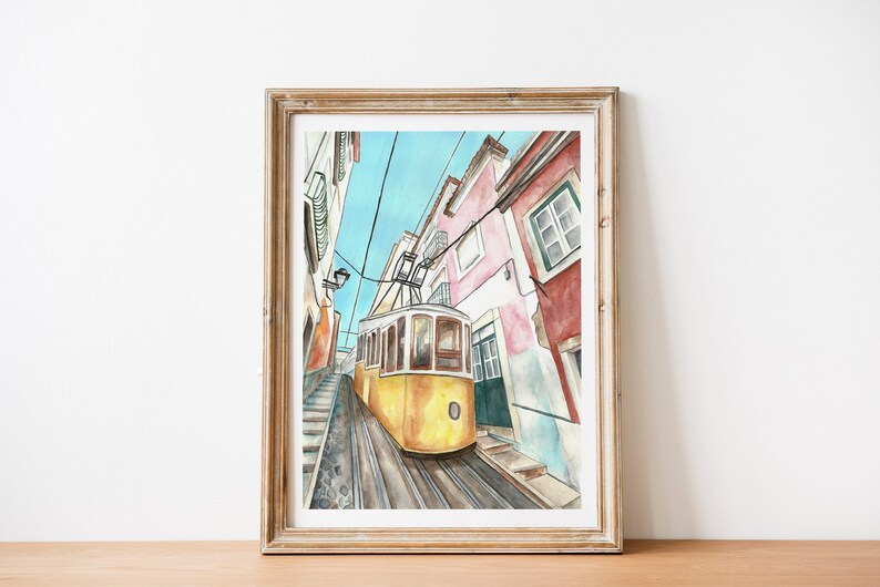 May include: A watercolor painting of a yellow tram traveling up a narrow street in Lisbon, Portugal. The buildings on either side of the street are painted in shades of pink, red, and white.