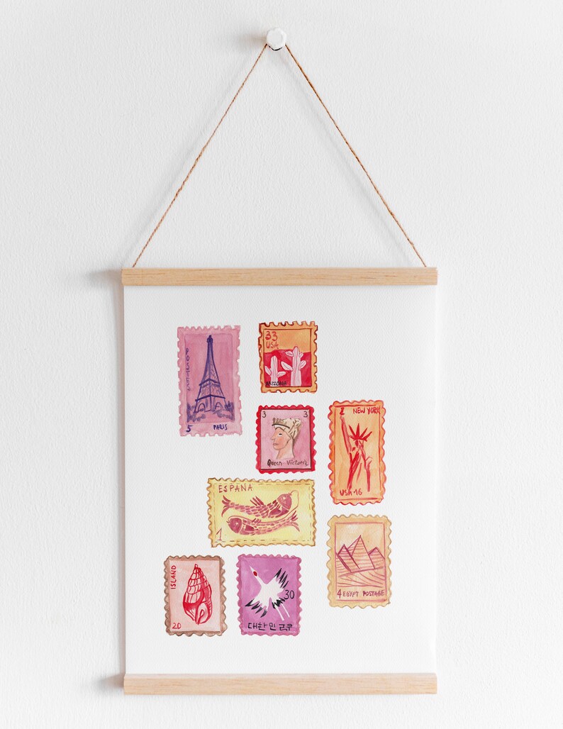 May include: Watercolor print featuring various postage stamps with travel-themed illustrations. The stamps depict landmarks like the Eiffel Tower, Statue of Liberty, and pyramids, along with other designs. The print is displayed on a white background and held by a wooden frame.