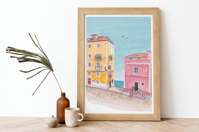 May include: A watercolor painting of two buildings, one yellow and one pink, with a blue sky and sea in the background.