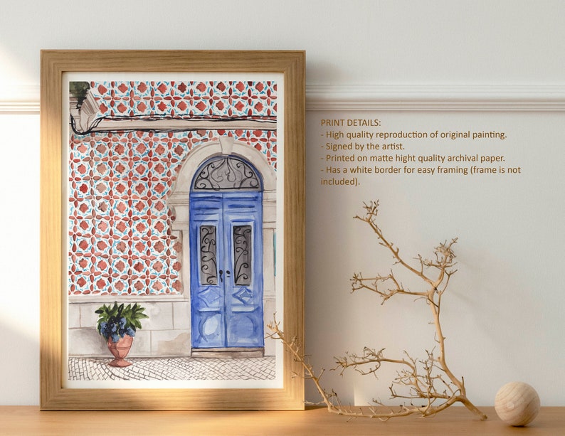 Puede incluir: Pintura acuarela de una puerta azul con una reja de hierro decorativa. La puerta est&aacute; ubicada en un edificio con azulejos de patrones rojos y blancos. La pintura est&aacute; enmarcada en un marco de madera claro.
