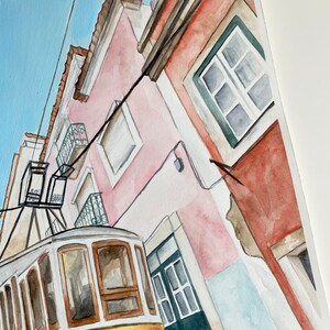 May include: Watercolor painting of a yellow tram traveling up a narrow street lined with pink and red buildings. The buildings have windows and doors, and the tram has a white roof and brown trim.
