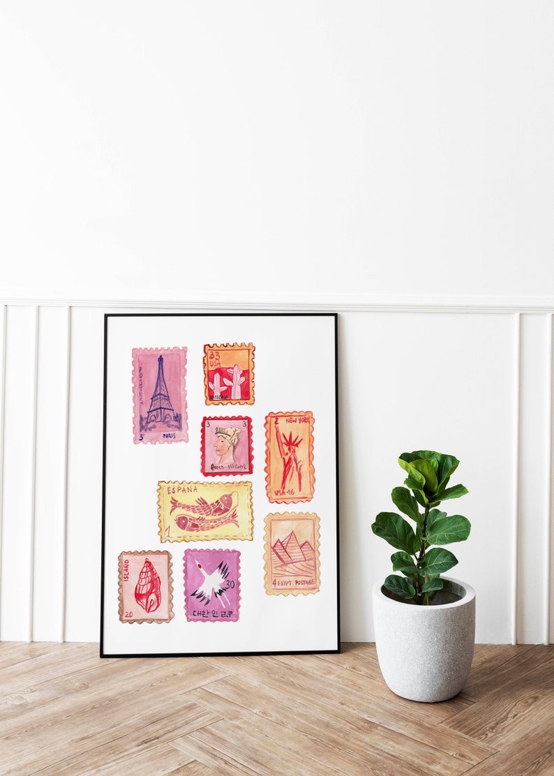 May include: A framed print featuring watercolor illustrations of postage stamps. The stamps depict landmarks like the Eiffel Tower and the Statue of Liberty, along with other designs. The print is displayed on a white wall next to a potted plant.