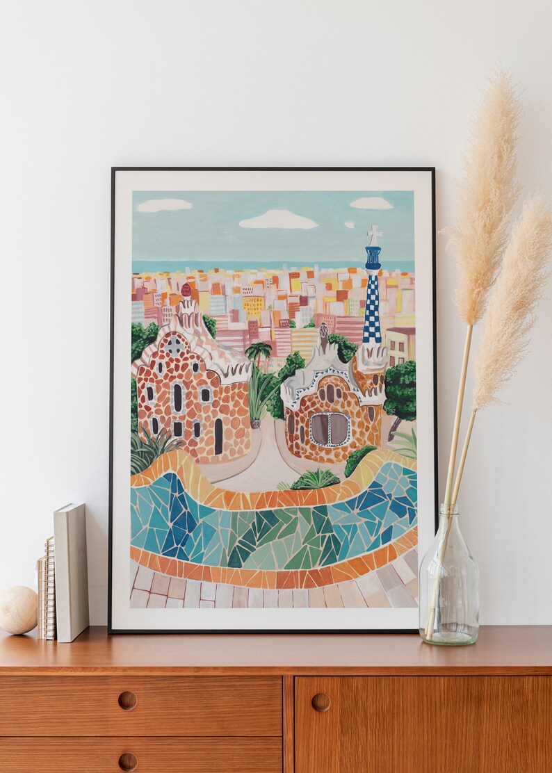 May include: A framed illustration of a colorful cityscape with a mosaic tiled pathway and a building with a unique architectural design. The illustration is in a black frame and is hanging on a white wall.