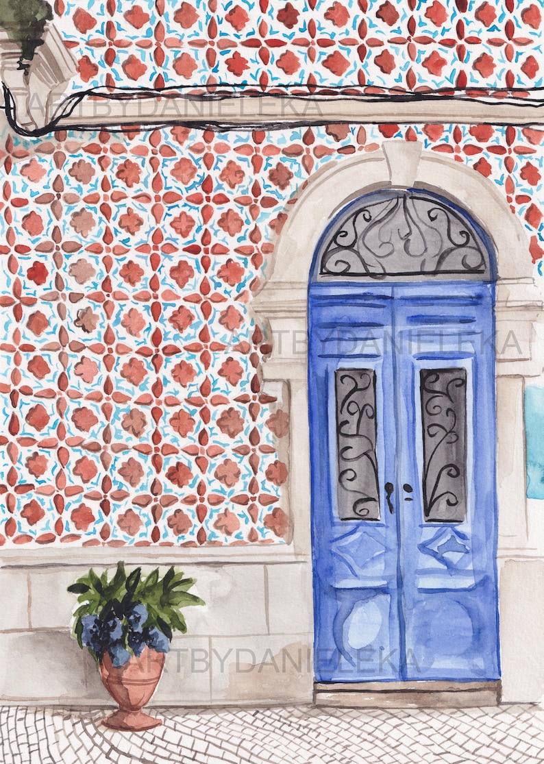Puede incluir: Una puerta doble azul con una reja de hierro decorativa y un arco blanco. La puerta est&aacute; situada contra una pared con un dise&ntilde;o de azulejos rojo y azul. Una planta en maceta con hojas verde oscuro y flores moradas se encuentra delante de la puerta.