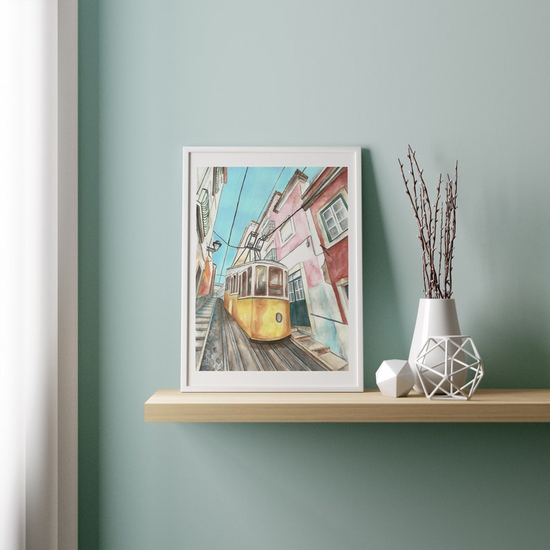 May include: A watercolor painting of a yellow tram traveling up a narrow street in Lisbon, Portugal. The buildings on either side of the street are painted in shades of pink, white, and blue.