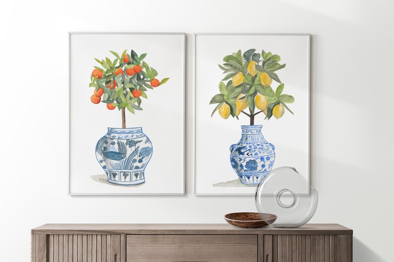 May include: Two watercolour paintings of potted citrus trees. The painting on the left features a small orange tree with orange fruit in a blue and white porcelain pot. The painting on the right features a lemon tree with yellow lemons in a blue and white porcelain pot.
