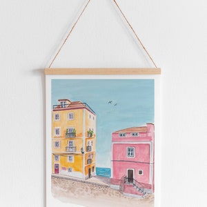 May include: A watercolor painting of two buildings, one yellow and one pink, with a blue sky and sea in the background.