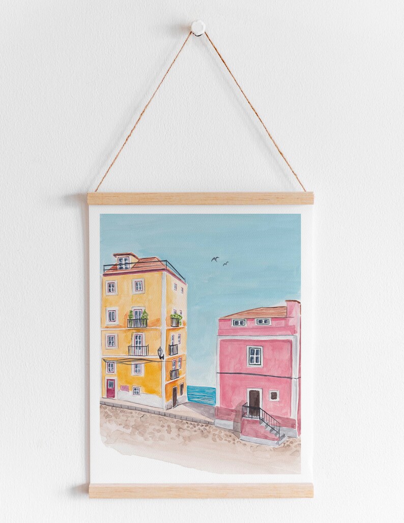 May include: A watercolor painting of two buildings, one yellow and one pink, with a blue sky and sea in the background.