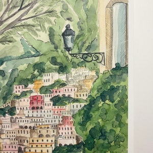 May include: Watercolour painting of a hillside town with colourful buildings and lush green trees. A street lamp is visible in the foreground.