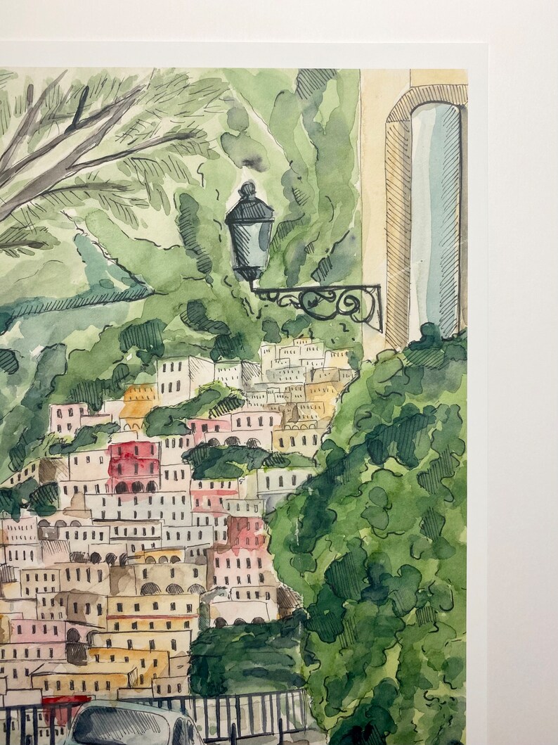 May include: Watercolour painting of a hillside town with colourful buildings and lush green trees. A street lamp is visible in the foreground.