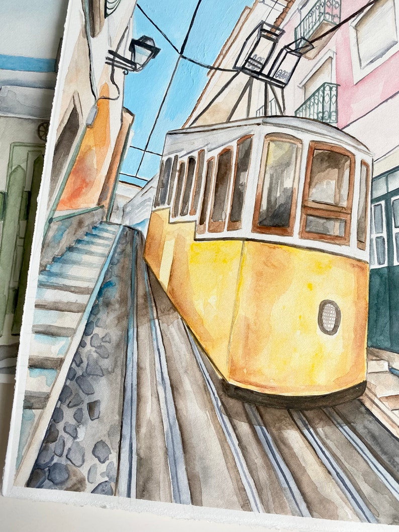 May include: Watercolor painting of a yellow tram traveling up a steep, cobblestone street in a city. The tram has large windows and a white roof. The street is lined with buildings on either side.