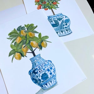 May include: Two watercolour paintings of potted citrus trees. The first painting features a small orange tree with orange fruit in a blue and white porcelain vase. The second painting features a lemon tree with yellow lemons in a blue and white porcelain vase.