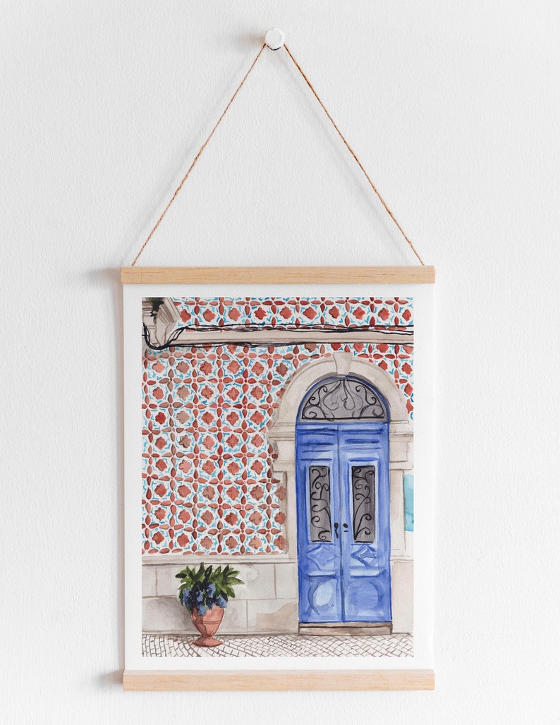 Puede incluir: Una pintura de acuarela de una puerta azul con intrincados trabajos en hierro, sobre un fondo de azulejos con patrones rojos y blancos. Una planta en maceta se encuentra a la izquierda de la puerta.
