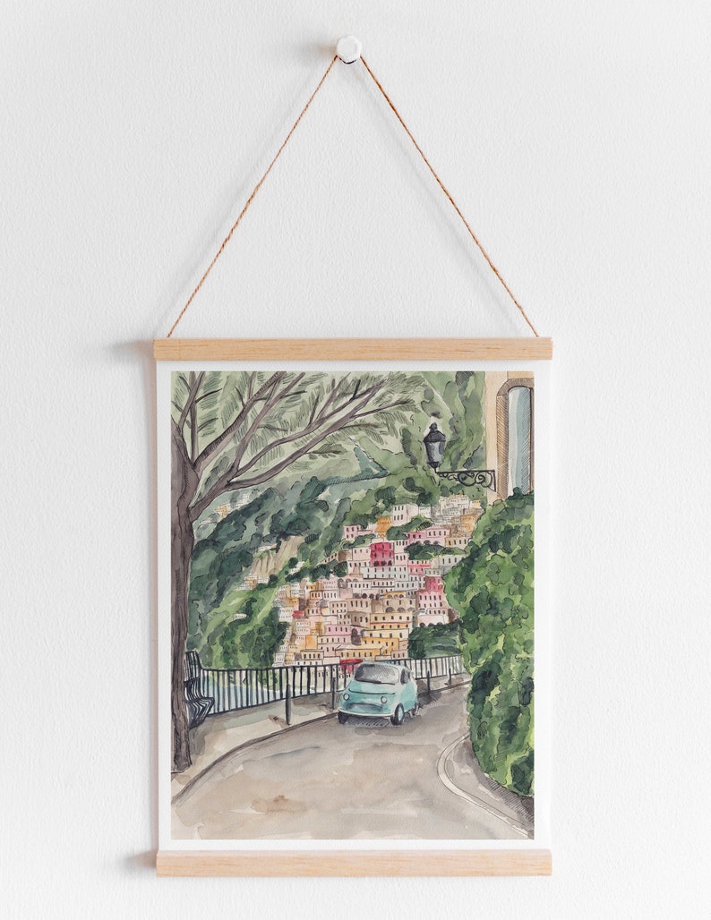 May include: A watercolour painting of a blue car driving on a winding road through a colourful village nestled in a hillside. Lush green trees and foliage surround the road and village.