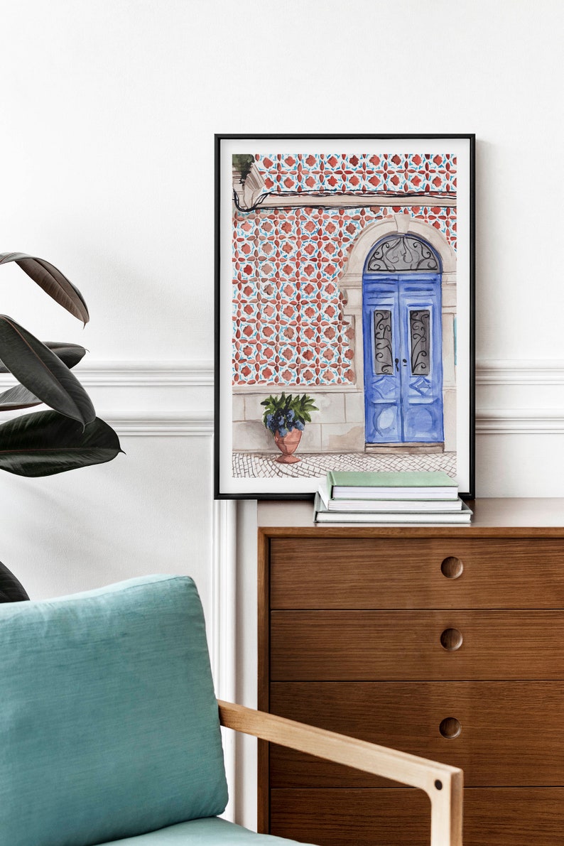 Puede incluir: Una pintura de acuarela enmarcada de una puerta azul con intrincados trabajos en hierro. La puerta est&aacute; situada contra una pared cubierta de azulejos con patrones rojos y blancos. Una planta en maceta se encuentra en el suelo frente a la puerta.