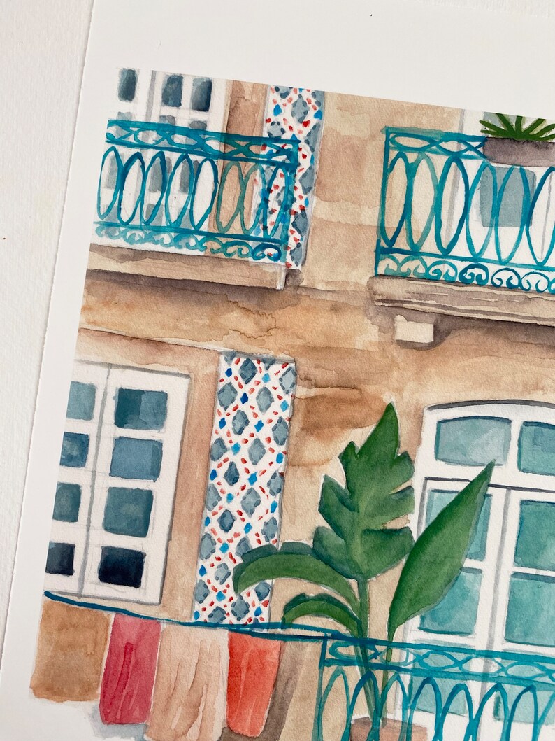 May include: Watercolour painting of a building with a balcony and a plant. The building is painted in shades of brown and beige, with blue tiled accents. The balcony has a blue railing and a plant in a terracotta pot. The painting is done in a realistic style.
