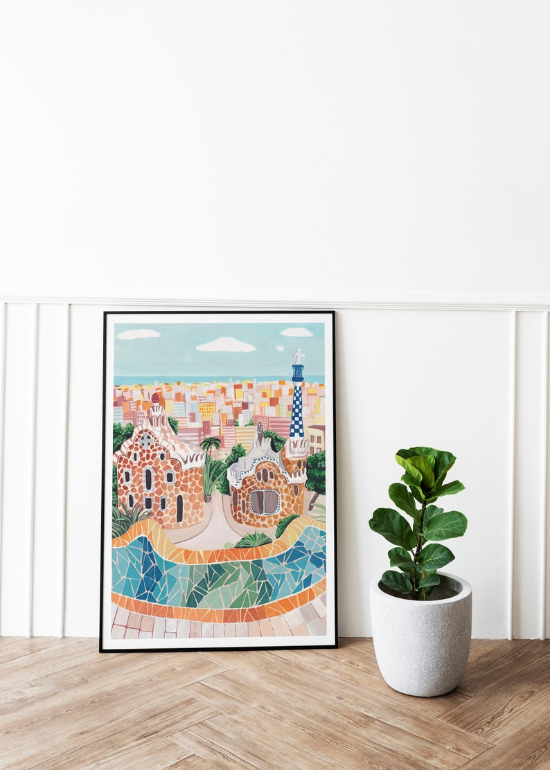 May include: A framed illustration of a colorful cityscape with a mosaic tiled walkway and two buildings with a unique architectural style. The buildings are brown with a textured surface and have a whimsical design. The cityscape is in the background and is a mix of yellow, orange, and white buildings.