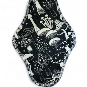 May include: A black reusable cloth menstrual pad with a white mushroom print. The pad has a white stitched border.