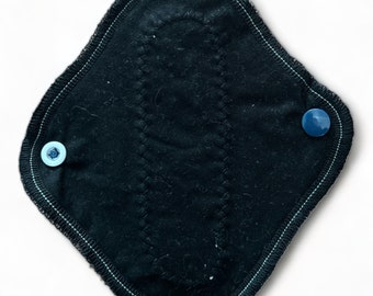May include: Black reusable cloth menstrual pad with a dark blue snap button on each side.