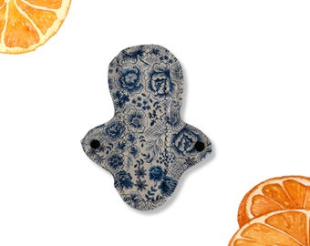 May include: A reusable cloth menstrual pad with a white background and a blue floral pattern. The pad has two black snaps on the sides.