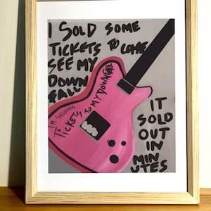 May include: Framed artwork with a pink electric guitar design. The artwork includes handwritten text: "I sold some tickets to come see my downfall" and "It sold out in minutes."