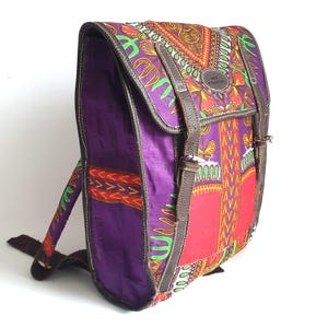 Puede incluir: Una colorida mochila con cierre de solapa. La bolsa presenta un patrón vibrante en rojo, morado, verde y naranja. Tiene detalles y correas de cuero marrón. La bolsa está diseñada con una forma rectangular y un asa superior.