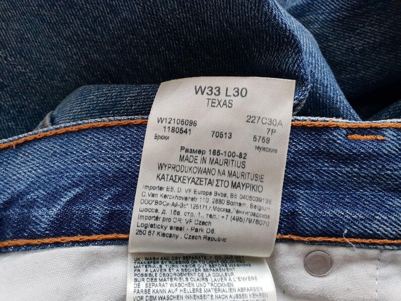 May include: Close-up of blue denim jeans with a white tag. The tag displays the size W33 L30, the word "TEXAS", and other details. The jeans have orange stitching.