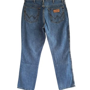 May include: A pair of blue denim jeans with a brown leather patch on the back pocket that says "Wrangler".