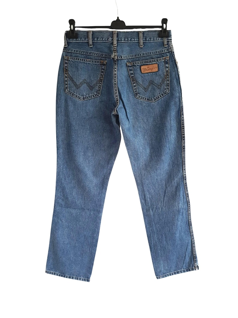 May include: A pair of blue denim jeans with a brown leather patch on the back pocket that says "Wrangler".