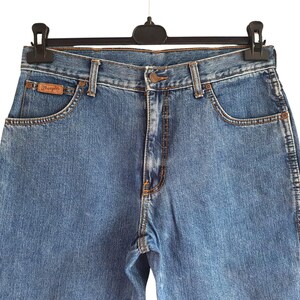 May include: A pair of blue denim jeans with a brown leather patch that says "Wrangler" on the back pocket.