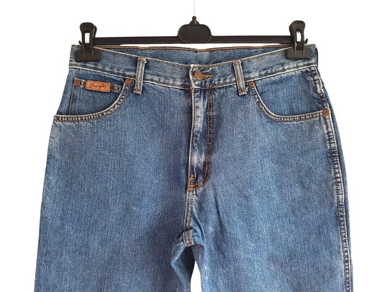 May include: A pair of blue denim jeans with a brown leather patch that says "Wrangler" on the back pocket.