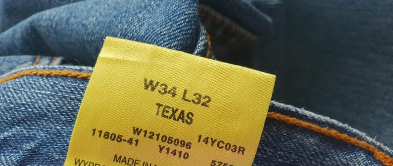 May include: A yellow tag with the text "W34 L32 TEXAS" and additional numbers and letters. The tag is attached to a pair of blue jeans.
