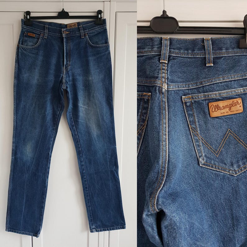 May include: A pair of blue denim jeans with a brown leather Wrangler label on the back pocket. The jeans have a classic straight leg style.