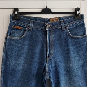 May include: A pair of blue denim jeans with a brown leather patch that says "Wrangler" on the back pocket.