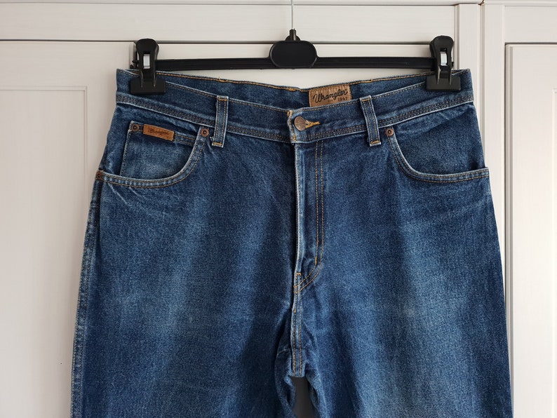 May include: A pair of blue denim jeans with a brown leather patch that says "Wrangler" on the back pocket.